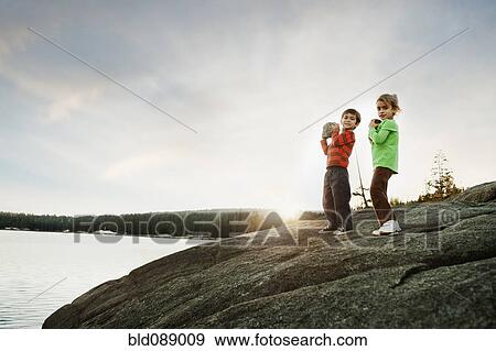 Stock Photo - Children holding rocks near remote lake. Fotosearch