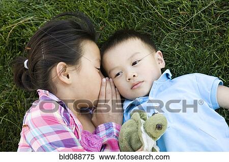 Stock Photography - Chinese girl laying in grass and whispering to brother. Fotosearch