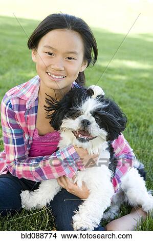Picture - Chinese girl sitting in grass with Shih Tzu dog. Fotosearch