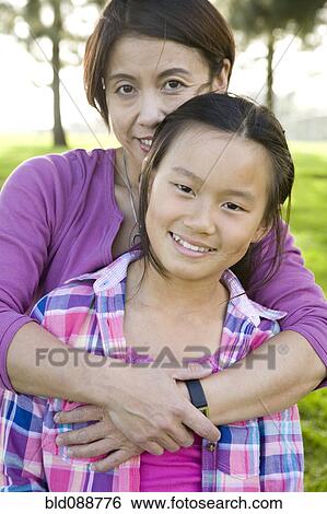 Stock Photograph - Chinese mother hugging daughter outdoors. Fotosearch