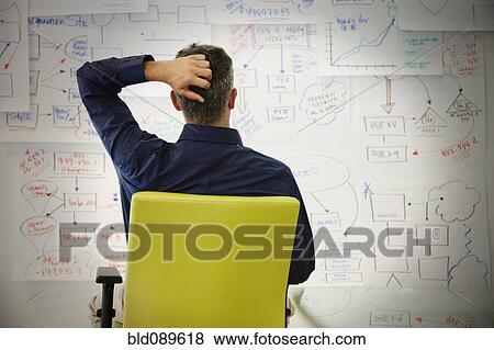 Stock Photo - Confused businessman looking at paper drawings. Fotosearch