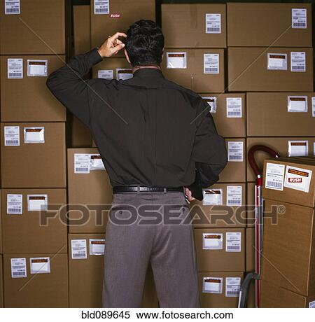 Stock Photography - Confused businessman standing with boxes. Fotosearch