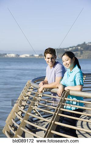 Stock Image - Couple leaning on railing at waterfront. Fotosearch
