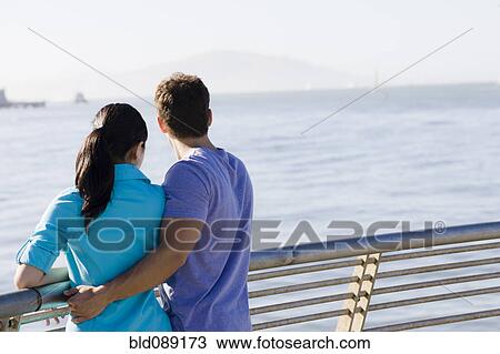 Stock Image - Couple leaning on railing at waterfront. Fotosearch