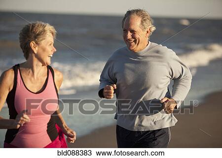 Stock Image - Couple running together on beach. Fotosearch