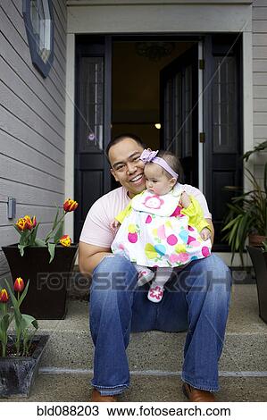Stock Image - Father sitting on front stoop with baby girl. Fotosearch