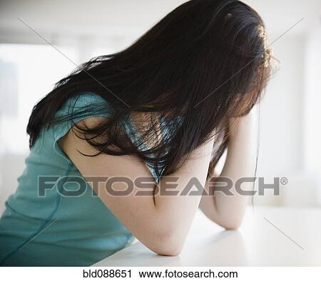 Stock Image - Frustrated Korean woman with head in hands. Fotosearch