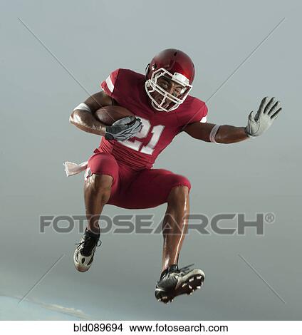 Grimacing Black football player carrying football in mid-air View Large Photo Image Picture - Grimacing Black football player carrying football in mid-air. Fotosearch
