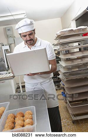 Hispanic baker working on laptop in commercial kitchen View Large Photo Image Stock Image - Hispanic baker working on laptop in commercial kitchen. Fotosearch