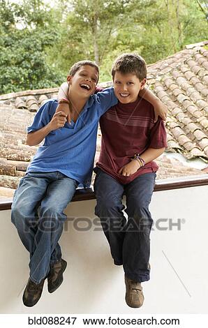 Stock Photo - Hispanic boys sitting on roof hugging. Fotosearch