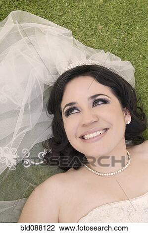 Stock Image - Hispanic bride laying in grass. Fotosearch