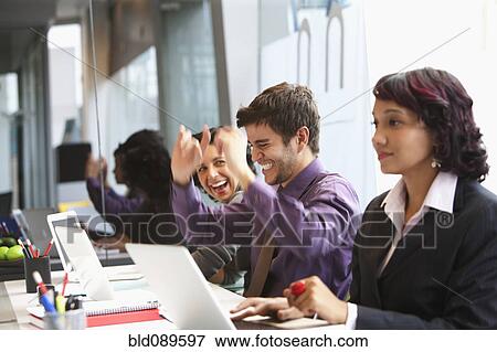 Stock Photo - Hispanic businessman laughing in office with co-workers. Fotosearch