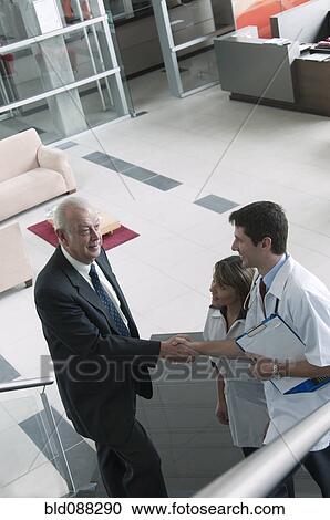 Stock Image - Hispanic businessman shaking hands with doctor on staircase. Fotosearch