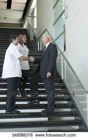 Hispanic businessman shaking hands with doctor on staircase View Large Photo Image Stock Photograph - Hispanic businessman shaking hands with doctor on staircase. Fotosearch