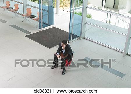 Stock Image - Hispanic businessman sitting and waiting in lobby. Fotosearch