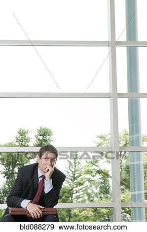 Stock Photo - Hispanic businessman sitting in lobby with briefcase. Fotosearch