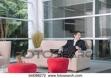 Stock Image - Hispanic businessman sitting on sofa waiting. Fotosearch