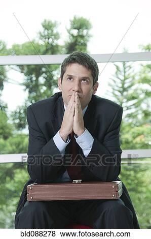 Stock Photo - Hispanic businessman sitting with briefcase praying. Fotosearch