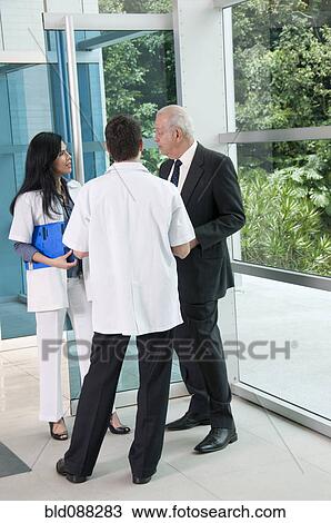 Stock Image - Hispanic businessman talking to doctor in lobby. Fotosearch