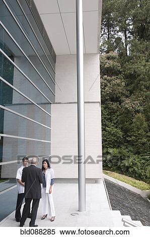 Stock Photography - Hispanic businessman talking to doctor outdoors. Fotosearch