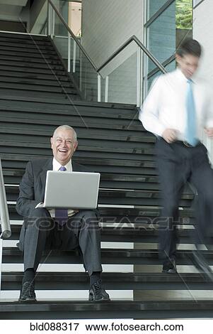 Stock Photo - Hispanic businessman using laptop on staircase. Fotosearch