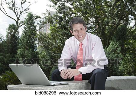 Stock Photo - Hispanic businessman using laptop outdoors. Fotosearch