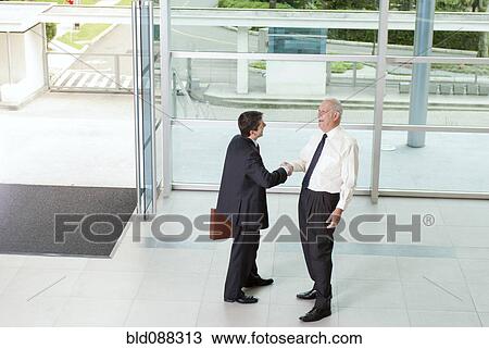 Stock Image - Hispanic businessmen shaking hands in lobby. Fotosearch