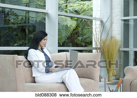 Hispanic businesswoman sitting on sofa typing on laptop View Large Photo Image Stock Photo - Hispanic businesswoman sitting on sofa typing on laptop. Fotosearch