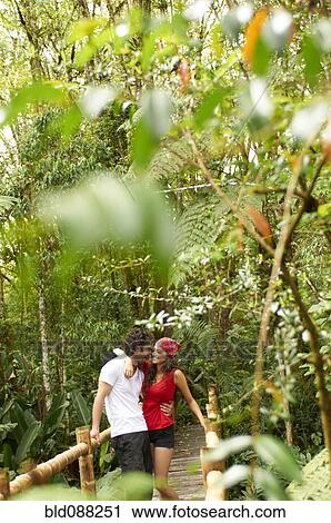 Stock Image - Hispanic couple hugging in forest on wooden walkway. Fotosearch