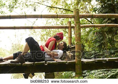 Stock Image - Hispanic couple laying together on wooden walkway. Fotosearch