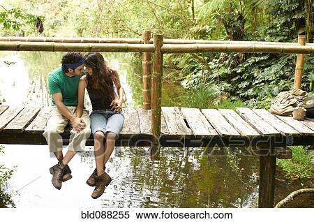 Stock Photography - Hispanic couple sitting holding hands on wooden walkway. Fotosearch