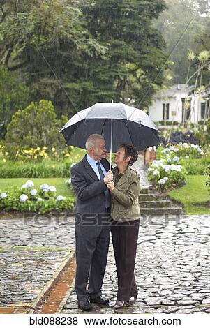 Stock Photo - Hispanic couple standing together under umbrella. Fotosearch