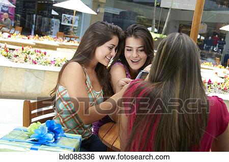 Stock Photograph - Hispanic friends text messaging on cell phone. Fotosearch