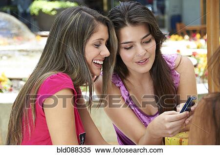 Stock Photography - Hispanic friends text messaging on cell phone. Fotosearch