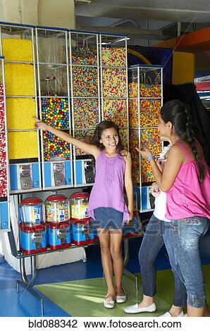 Stock Image - Hispanic girls looking at candy dispensers. Fotosearch