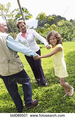 Stock Image - Hispanic grandparents holding hands with granddaughter. Fotosearch