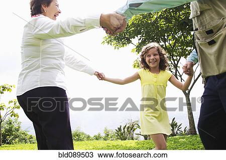 Stock Image - Hispanic grandparents holding hands with granddaughter. Fotosearch