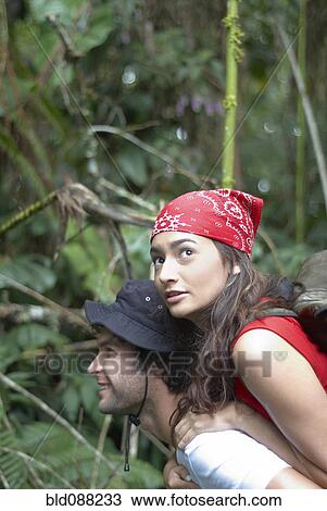 Stock Image - Hispanic man giving girlfriend piggyback ride in forest. Fotosearch