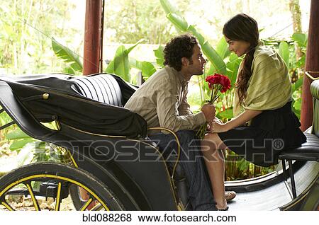 Stock Photo - Hispanic man sitting in carriage giving girlfriend roses. Fotosearch