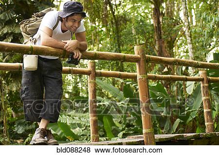 Stock Photo - Hispanic man with backpack standing on wooden walkway. Fotosearch