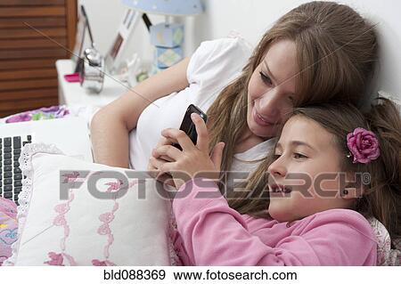 Stock Photo - Hispanic mother and daughter looking at cell phone. Fotosearch
