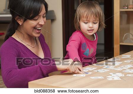 Stock Photo - Hispanic mother and daughter playing card game. Fotosearch