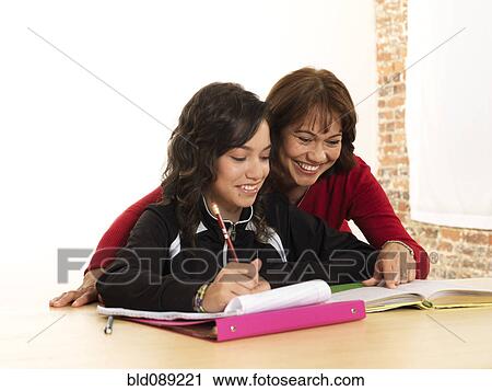 Stock Image - Hispanic mother helping daughter with homework. Fotosearch
