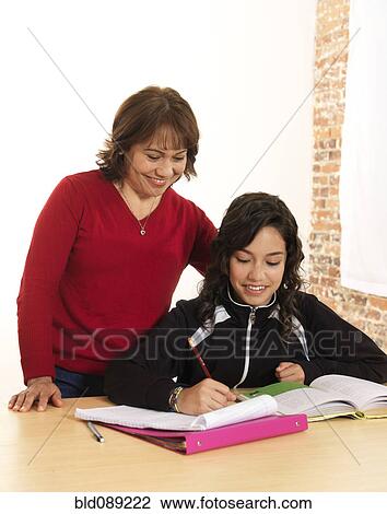 Stock Image - Hispanic mother helping daughter with homework. Fotosearch