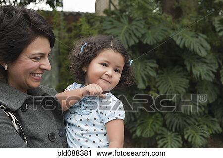 Stock Image - Hispanic mother holding daughter outdoors. Fotosearch