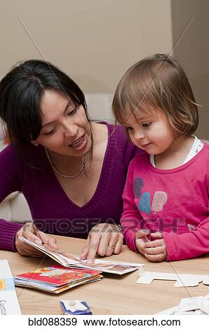 Stock Photo - Hispanic mother reading book to daughter. Fotosearch