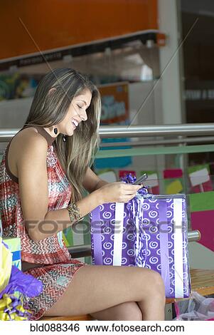Stock Photograph - Hispanic woman holding gift and using cell phone. Fotosearch