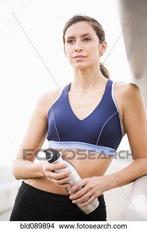 Picture - Hispanic woman in sportswear holding water bottle. Fotosearch