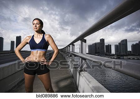 Stock Photograph - Hispanic woman in sportswear standing near urban waterfront. Fotosearch