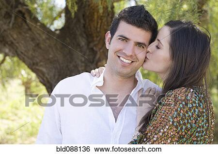 Stock Photograph - Hispanic woman kissing boyfriend outdoors. Fotosearch